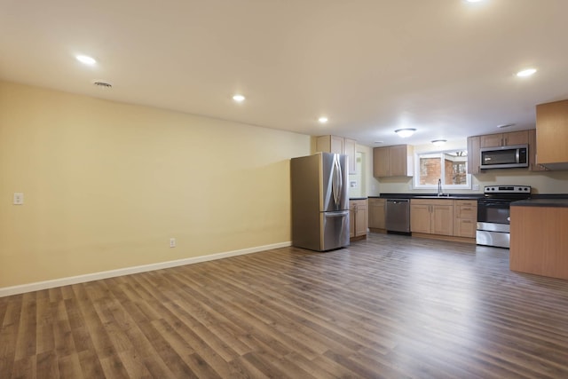 kitchen featuring dark countertops, a sink, stainless steel appliances, open floor plan, and dark wood-type flooring