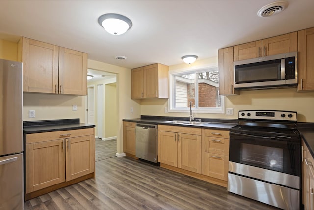kitchen featuring a sink, appliances with stainless steel finishes, dark countertops, and dark wood-type flooring