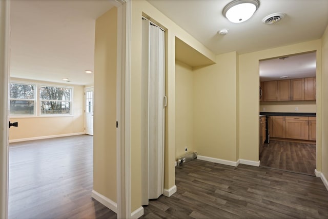 hall featuring baseboards, visible vents, and dark wood-type flooring