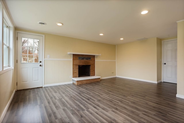 unfurnished living room featuring a brick fireplace, recessed lighting, baseboards, visible vents, and dark wood-style floors