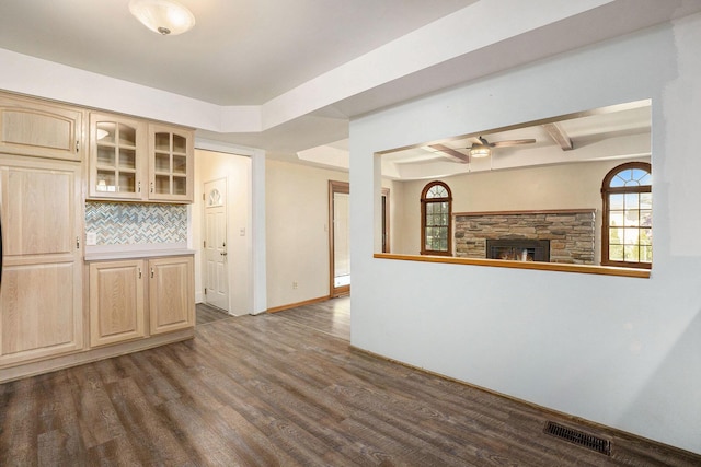 interior space with a fireplace, dark wood-type flooring, backsplash, visible vents, and glass insert cabinets