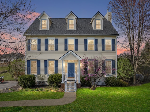 view of front of house with a shingled roof, a chimney, and a yard