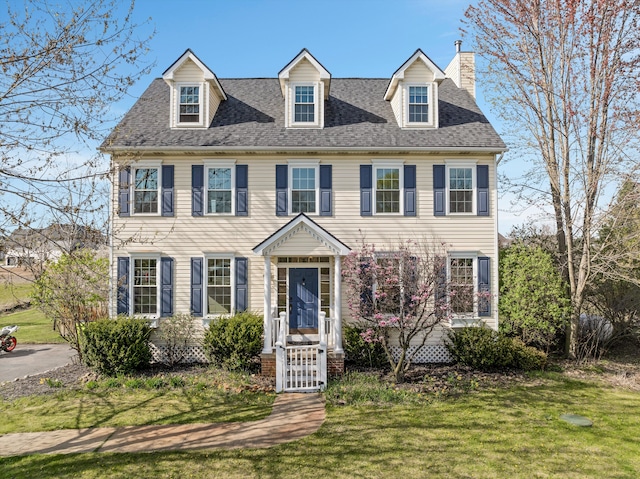 colonial home featuring a shingled roof, a chimney, and a front lawn