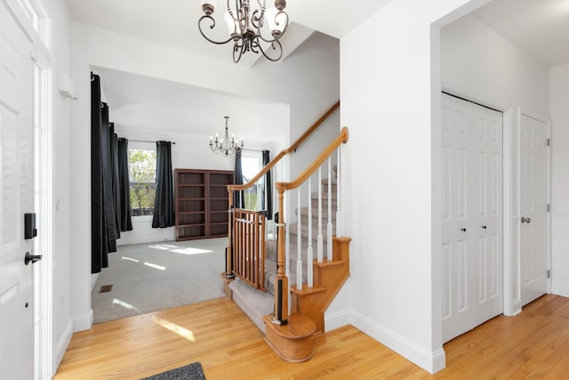 foyer entrance featuring baseboards, a chandelier, wood finished floors, and stairway