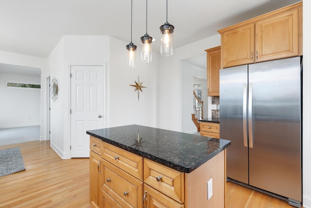 kitchen featuring dark stone counters, a kitchen island, light wood finished floors, and stainless steel refrigerator