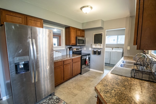 kitchen featuring brown cabinets, a sink, baseboards, stainless steel appliances, and washer and dryer