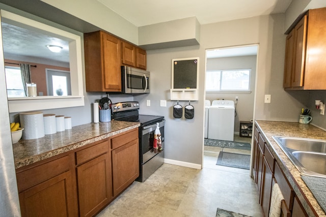 kitchen with brown cabinetry, baseboards, washer and clothes dryer, a sink, and appliances with stainless steel finishes