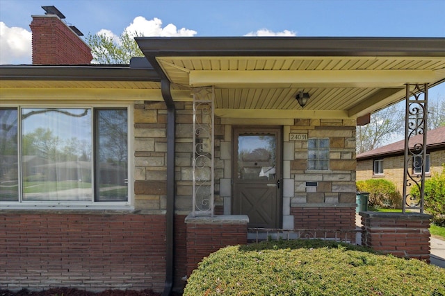 doorway to property featuring a chimney, brick siding, and stone siding