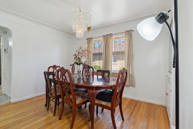 dining area featuring arched walkways, baseboards, an inviting chandelier, and light wood-style flooring