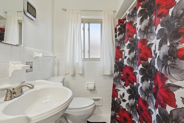 bathroom featuring a shower with curtain, tile walls, a sink, a wainscoted wall, and toilet