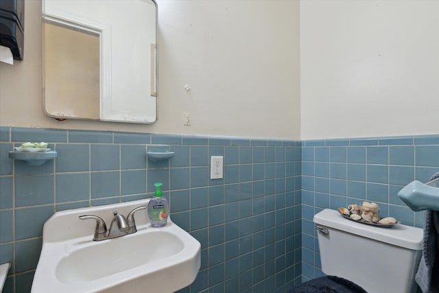 half bath with a sink, tile walls, wainscoting, and toilet