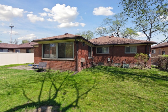 rear view of property with brick siding, fence, and a yard