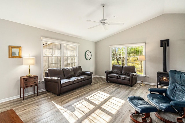 living area featuring ceiling fan, vaulted ceiling, a wood stove, baseboards, and light wood-style floors