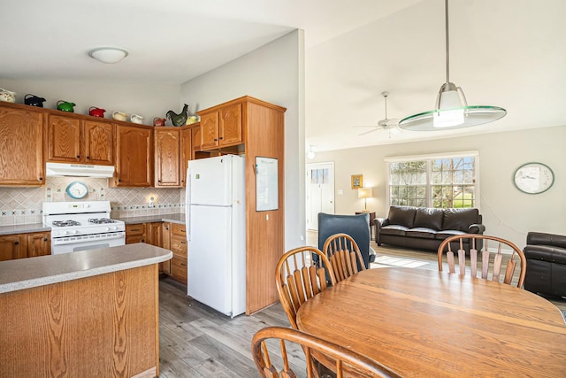 kitchen featuring light wood finished floors, vaulted ceiling, white appliances, and under cabinet range hood