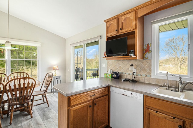 kitchen featuring a peninsula, lofted ceiling, white dishwasher, light wood-type flooring, and tasteful backsplash