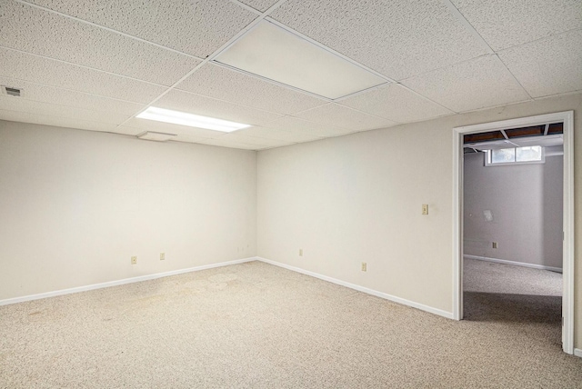 basement featuring baseboards, light colored carpet, and a drop ceiling