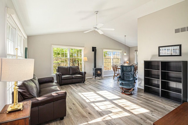 living room featuring visible vents, a wood stove, lofted ceiling, wood finished floors, and a ceiling fan