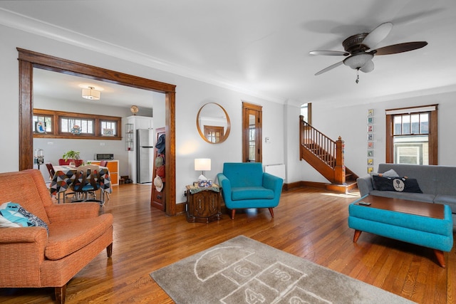 living room featuring crown molding, stairs, a ceiling fan, baseboards, and wood finished floors