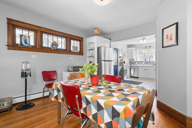 dining area featuring baseboards, a baseboard heating unit, and light wood finished floors