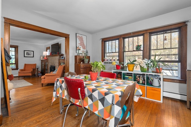 dining area with plenty of natural light, a brick fireplace, baseboard heating, and hardwood / wood-style flooring