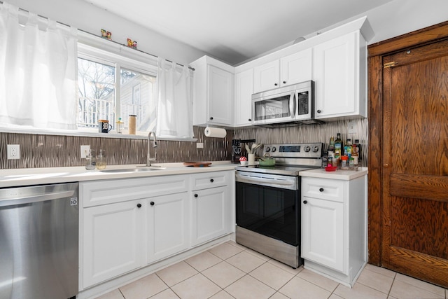 kitchen with light countertops, white cabinets, a sink, appliances with stainless steel finishes, and light tile patterned floors
