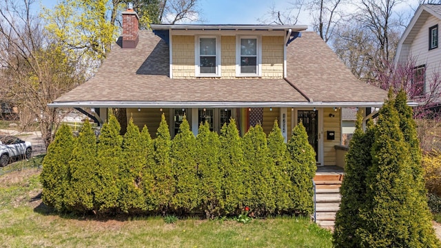 view of front facade featuring covered porch, a chimney, and roof with shingles