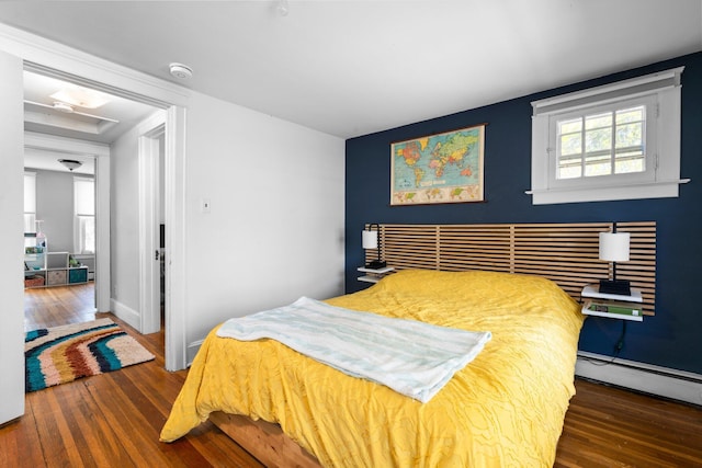 bedroom featuring baseboards, a baseboard heating unit, and wood finished floors
