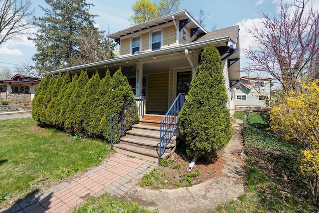 view of front of house with covered porch, a shingled roof, and a front yard