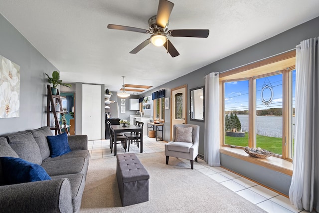 living area with a water view, a ceiling fan, and light tile patterned flooring