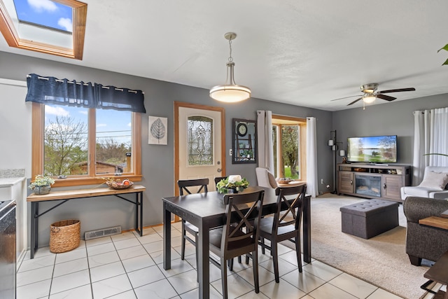 dining room featuring visible vents, light carpet, a ceiling fan, light tile patterned floors, and a skylight