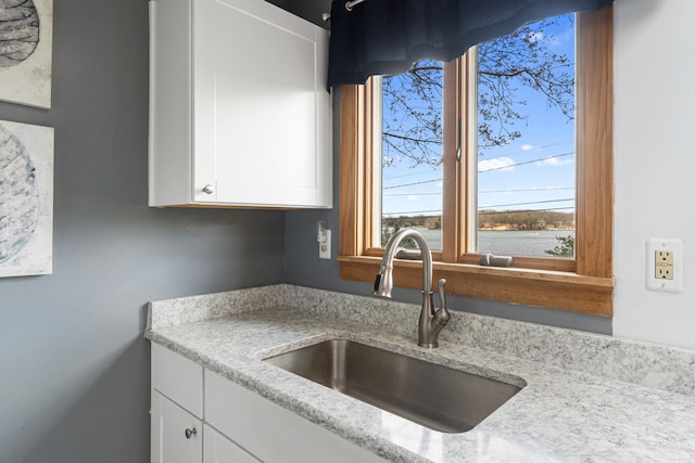 kitchen with white cabinetry, light stone countertops, plenty of natural light, and a sink