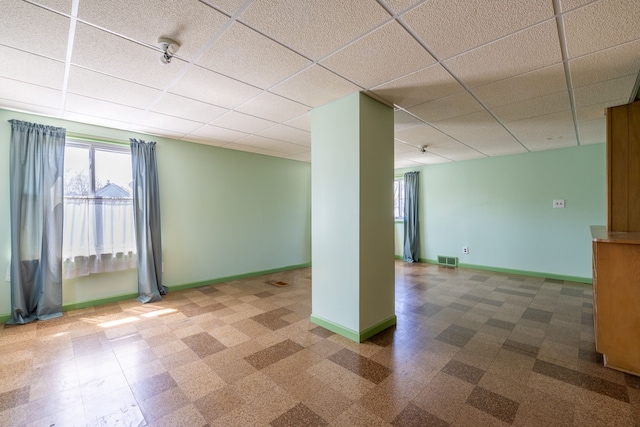 below grade area with baseboards, a drop ceiling, tile patterned floors, and visible vents