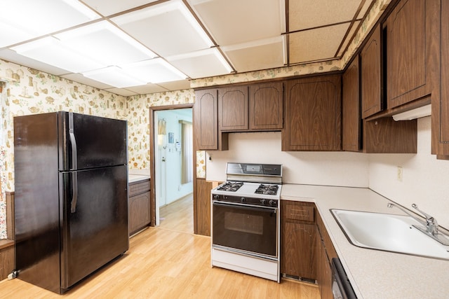 19302 Moross Rd, Detroit, MI 48224 - kitchen featuring freestanding refrigerator, gas range, wallpapered walls, a sink, and light wood-type flooring