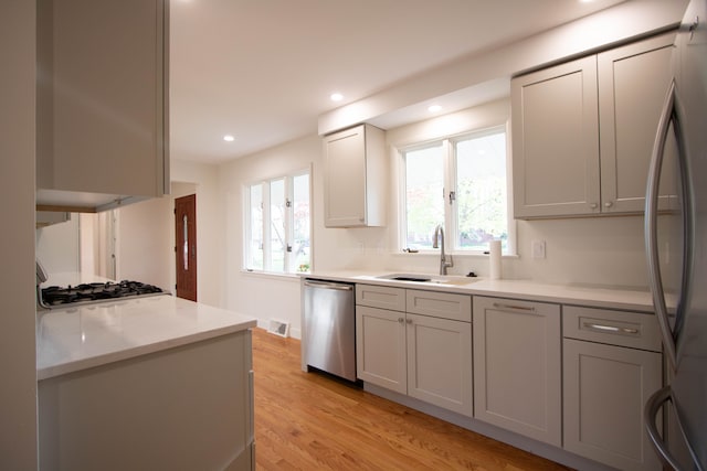 kitchen with appliances with stainless steel finishes, a sink, light countertops, recessed lighting, and light wood-style flooring