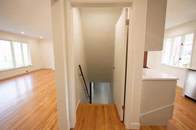 corridor with visible vents, light wood finished floors, baseboards, and an upstairs landing