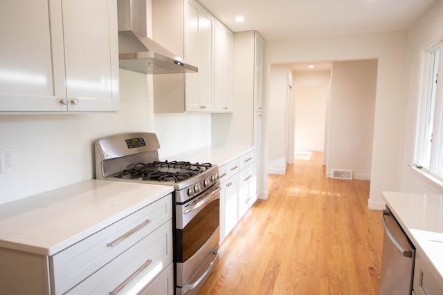 kitchen featuring visible vents, appliances with stainless steel finishes, light wood-type flooring, light countertops, and wall chimney exhaust hood