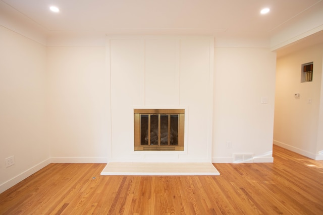 unfurnished living room featuring a glass covered fireplace, baseboards, light wood-style flooring, and visible vents