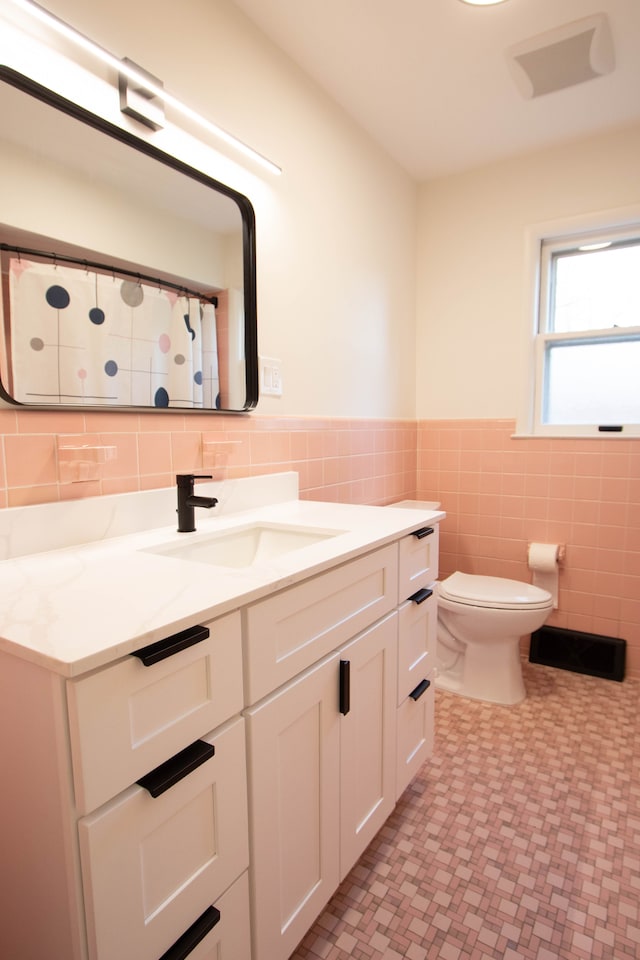 full bath with wainscoting, vanity, toilet, tile patterned floors, and tile walls