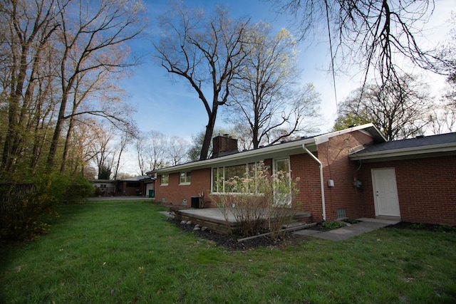 rear view of house featuring a yard, brick siding, and a chimney
