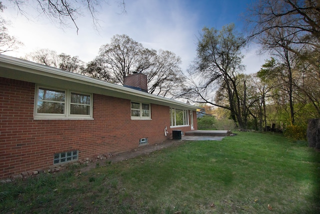 view of side of home featuring a chimney, a patio area, central air condition unit, brick siding, and a yard