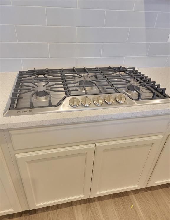 interior details with light wood-type flooring, decorative backsplash, stainless steel gas cooktop, and light stone countertops