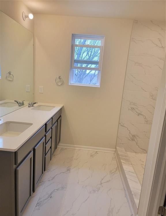 full bath with a sink, baseboards, double vanity, and marble finish floor