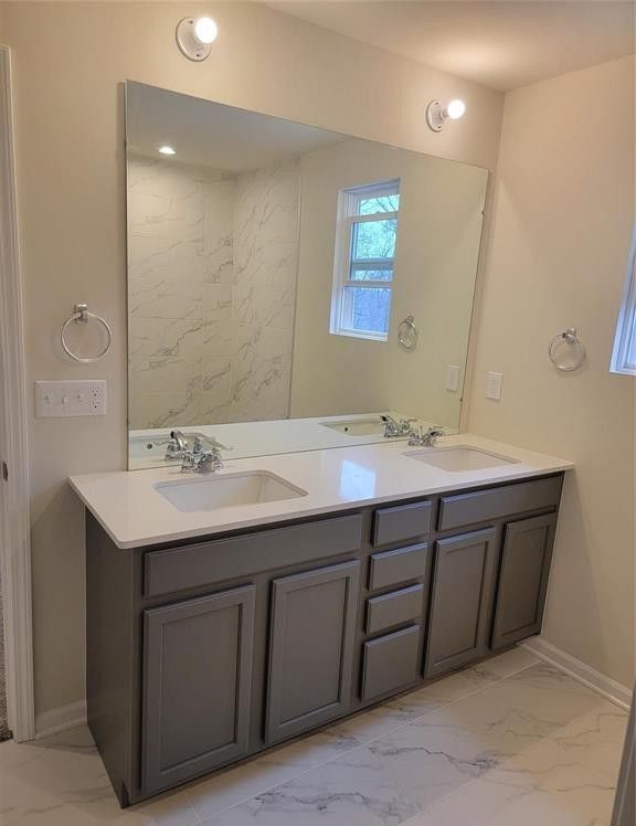 full bathroom featuring double vanity, baseboards, a sink, and marble finish floor