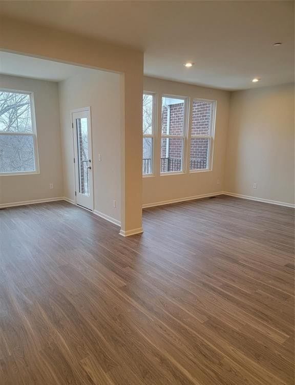 unfurnished living room with baseboards, dark wood-style floors, and plenty of natural light