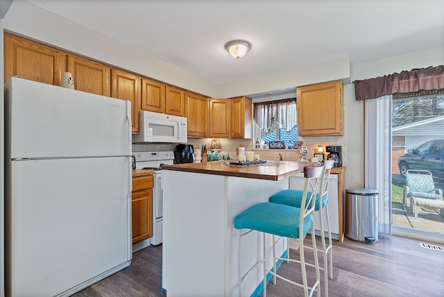 kitchen with visible vents, white appliances, a kitchen breakfast bar, dark wood finished floors, and backsplash