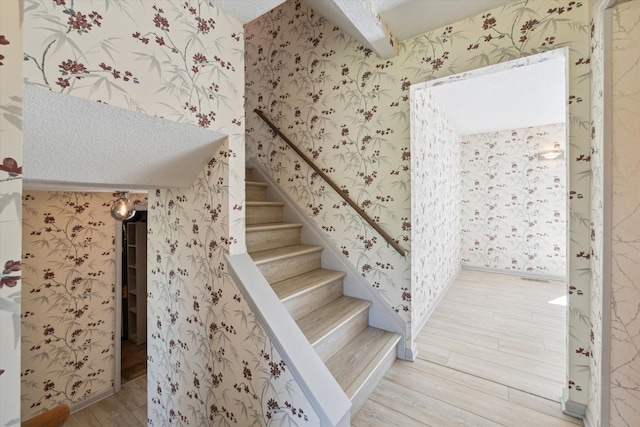 stairway featuring a textured ceiling, wallpapered walls, and wood finished floors