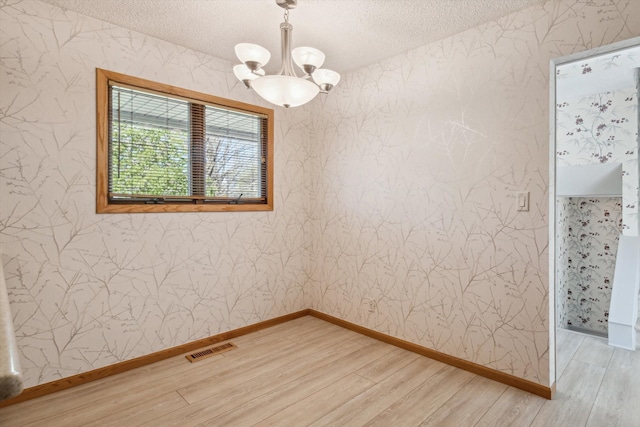 spare room with visible vents, light wood-style floors, wallpapered walls, a textured ceiling, and a chandelier