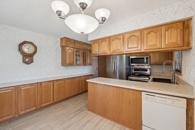 kitchen featuring a textured ceiling, appliances with stainless steel finishes, a sink, light countertops, and wallpapered walls