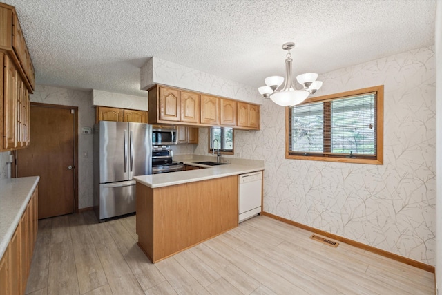 kitchen featuring appliances with stainless steel finishes, a sink, a textured ceiling, wallpapered walls, and light wood-type flooring