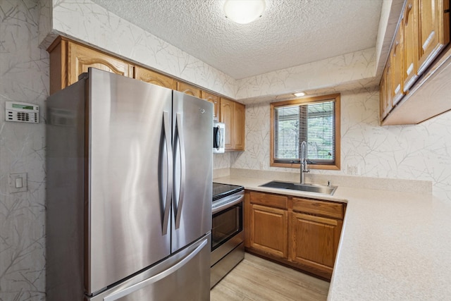 kitchen featuring a sink, light countertops, a textured ceiling, light wood-style flooring, and stainless steel appliances